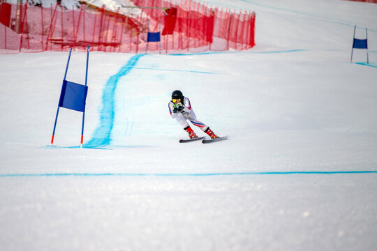 alpine ski athlete racing downhill on snowy ski slope passing blue gate