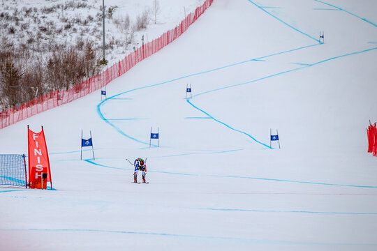 alpine ski athlete racing downhill on snowy ski slope passing finish line
