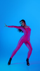 Dancer in vibrant pink bodysuit strikes pose with blue background. Concept of dance brand,...