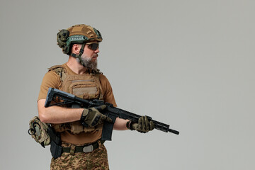 A soldier in military uniform holds a rifle AR 15 in his hands on grey background in studio