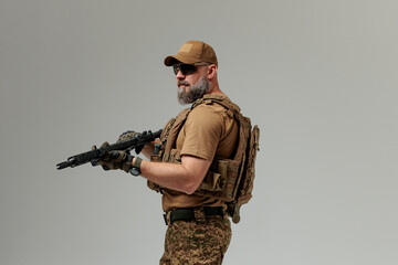 A soldier in military uniform holds a rifle AR 15 in his hands on grey background in studio