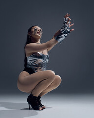 Energetic dancer in metallic attire strikes jazz funk pose wearing high heels. Concept of bold...