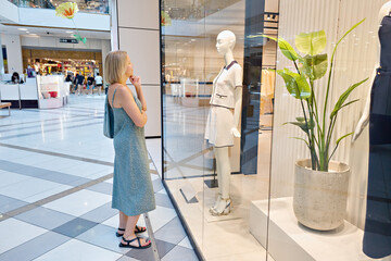 Naklejka na ściany i meble Girl looks into a clothing store window