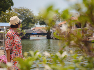 Young woman in ethnic dress and hat exploring the vibrant streets of Malacca, Malaysia. A blend of...
