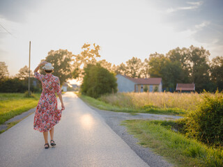 Young woman walking through picturesque European field in late summer. Golden sunlight, lush...