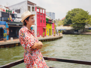 Young woman in ethnic dress and hat exploring the vibrant streets of Malacca, Malaysia. A blend of...
