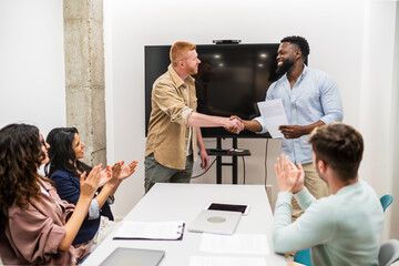 Two managers shaking hands after signing contract with their team applauding in modern coworking...