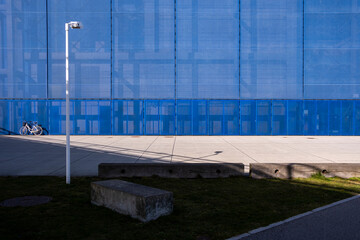 Blue glass facade with open paved plaza and bench, blending transparency and structure in an urban business district, excellent for generic urban context and design flexibility