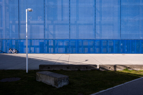 Blue glass facade with open paved plaza and bench, blending transparency and structure in an urban business district, excellent for generic urban context and design flexibility