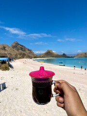Hand holding Flores black coffee with beautiful pink beach view.