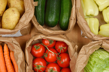 A top-down view shows multiple brown paper bags, each filled with various fresh vegetables including potatoes, zucchini, bell peppers, carrots, tomatoes, and lettuce