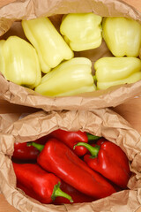 A top-down view shows two brown paper bags, one filled with pale green bell peppers and the other with vibrant red peppers, on a wooden surface
