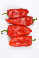 Four fresh, vibrant red peppers with green stems are arranged vertically on a plain light gray background, viewed from directly above