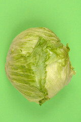A vibrant, whole head of crisp green iceberg lettuce is positioned centrally on a solid green...