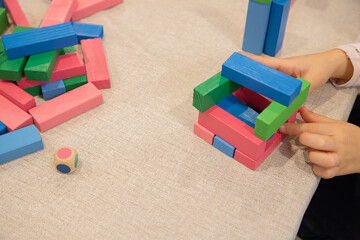 A young child plays indoors during the day, focusing intently while building a structure with colorful wooden blocks, developing fine motor skills, creativity, and early cognitive abilities.