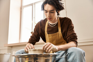 Creative expression in pottery studio with a stylish man shaping clay on the wheel