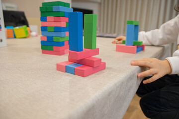 A young child plays indoors during the day, focusing intently while building a structure with colorful wooden blocks, developing fine motor skills, creativity, and early cognitive abilities.