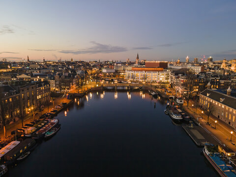 Aerial view of the tranquil canal reflecting the soft glow of streetlights and buildings, with the iconic Royal Theatre Carr&Atilde;&copy; standing majestically, Amsterdam, North Holland, Netherlands.