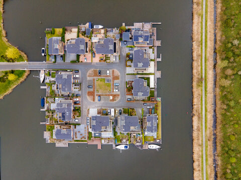 Aerial view of modern houses with dark roofs, surrounded by dark water and a light-colored pathway, creating a striking contrast, Amsterdam, North Holland, Netherlands.