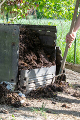 Homme avec une fourche creusant un bac à compost de jardin extérieur rempli de déchets alimentaires. Promouvoir le recyclage durable et les pratiques de compostage domestique.