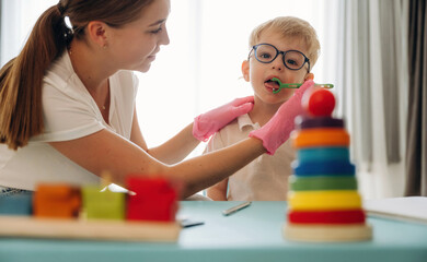 Exercises, using special device on tongue. Speech therapist is with young boy indoors