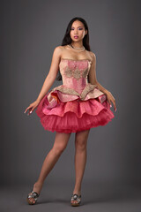Naklejka premium Beautiful brunette Asian woman with exquisite makeup and manicure in a pink short dress on a gray background