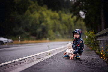 Young Boy Sitting on Wet Roadside During Rainy Day