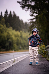 Young Boy Standing on Wet Roadside in Rain Gear
