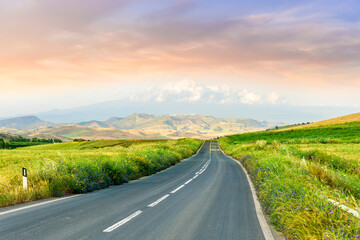 beautiful landscape of long road to amazing mountain scene from a green summer fields and hills. Asphalt road to mountains and golden meadows.