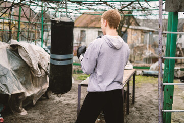 Young person in boxing gloves training with a punching bag outdoors. This image captures dedication and an active lifestyle, perfect for themes of fitness, sport, and personal development.