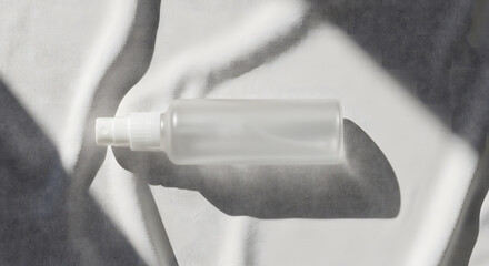 A clear, transparent spray bottle sits in bright sunlight, casting shadows.