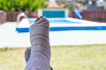 Close-up showcases an injured foot wrapped in a bandage, positioned near a blurred swimming pool in the background, highlighting the concepts of injury, insurance, and travel