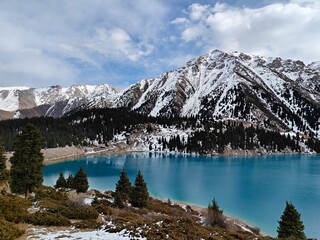 Stunning turquoise lake surrounded by snowy mountains and evergreen trees in the Kazakh landscape