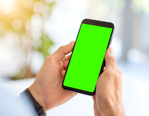 Close-up of hands holding a black smartphone with a green screen, blurred bright background.