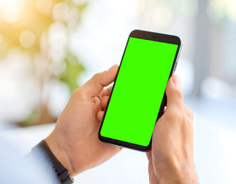 Close-up of hands holding a black smartphone with a green screen, blurred bright background. - Powered by Adobe
