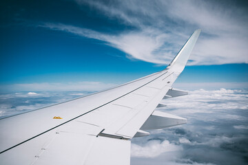 Modern airplane wing with winglet above white clouds and turquoise tones, captured mid-flight at high altitude, suggesting innovation and sustainable travel.