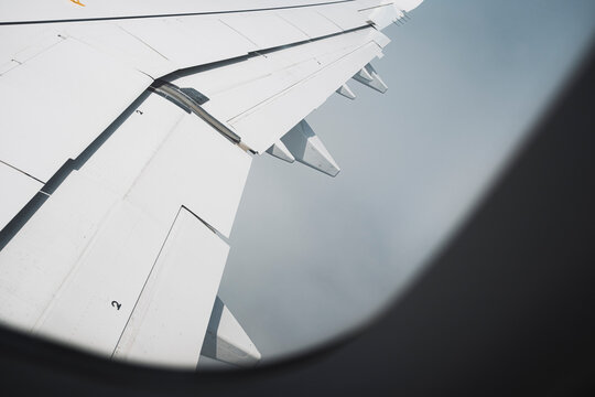 Wing of airplane seen through fogged window during ascent, atmospheric conditions and white tones dominating the view, abstract concept of flight and altitude.