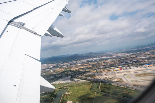 Airplane wing and flaps during landing approach, aerial view of urban and rural landscape beneath cloudy sky, motion and speed in commercial aviation.