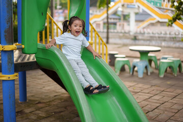 happy toddler baby girl sliding and playing at playground