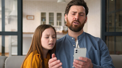 Disappointed Caucasian family guy man parent father holding mobile phone bad result girl kid problem negative sms at home upset child little daughter looking screen male dad failure online tech error