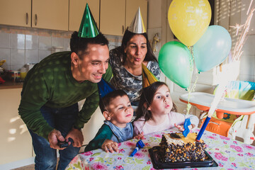 Family celebrating daughter's third birthday with cake and balloons
