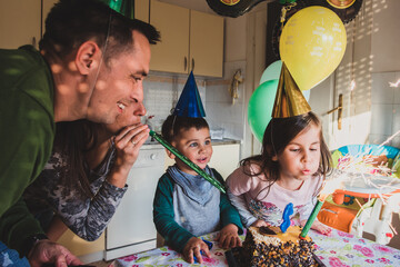 Family celebrating birthday with cake, balloons, and party hats