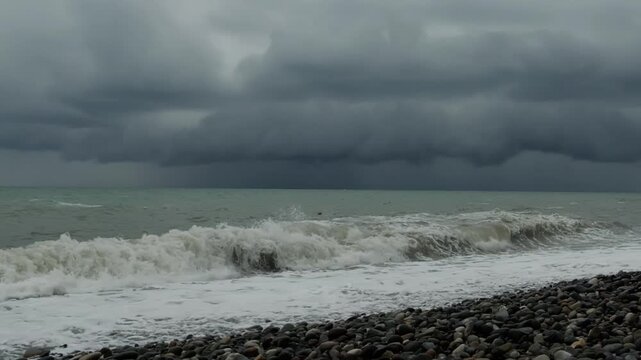 The stormy sky over the rocky seashore is a dramatic stormy landscape with heavy clouds in sea in overcast weather on pubble beach.. Waves washing stones on coastline. Slow motion cinematic shot.