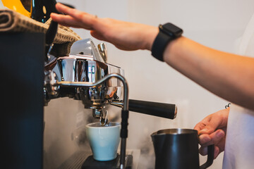 Close-up of a barista brewing espresso with steam rising from a professional machine, holding a milk pitcher and pouring into a white ceramic cup.