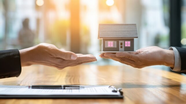 The hands exchanging a miniature house in a business transaction context.