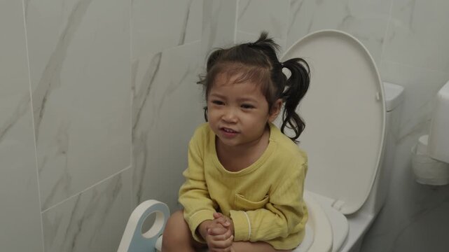 toddler girl sitting on a toilet at home and suffering from stomachache and constipation