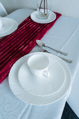 The beautifully set table features crisp white plates, elegant cups, shiny silverware, and a vibrant red table runner that brings a pop of color to the dining experience