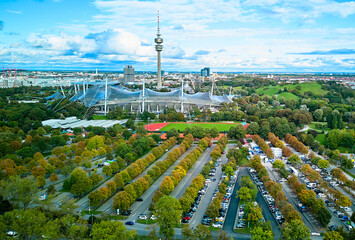 MÃ¼nchen, Germany - 10 February 2024: Aerial view of the Olympic Stadium, a landmark of architectural design, sits nestled amidst lush greenery, contrasting with the sleek lines of the Olympic Tower.