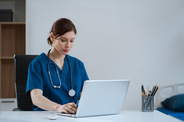 Doctor working with laptop computer and writing on paperwork.