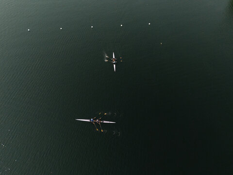 Aerial view of rowing boats cutting through the dark, shimmering waters of Lake Galve, leaving trails of light foam in their wake, Trakai, Vilnius country, Lithuania.